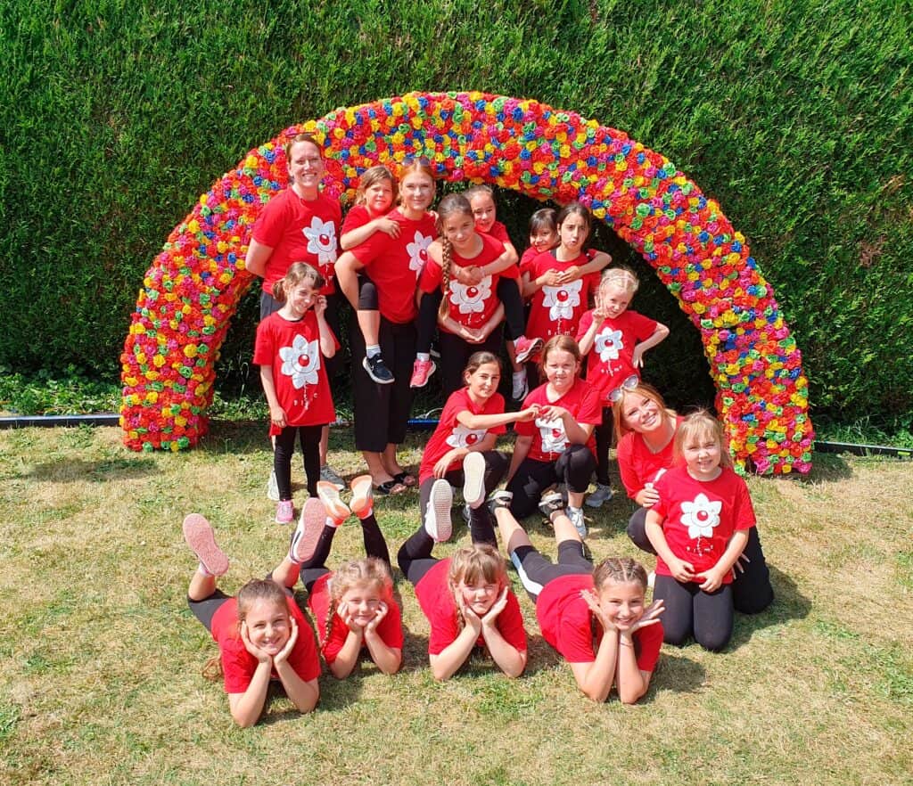 Gruppe von Kindern in roten T-Shirts vor buntem Blumenbogen im Garten.