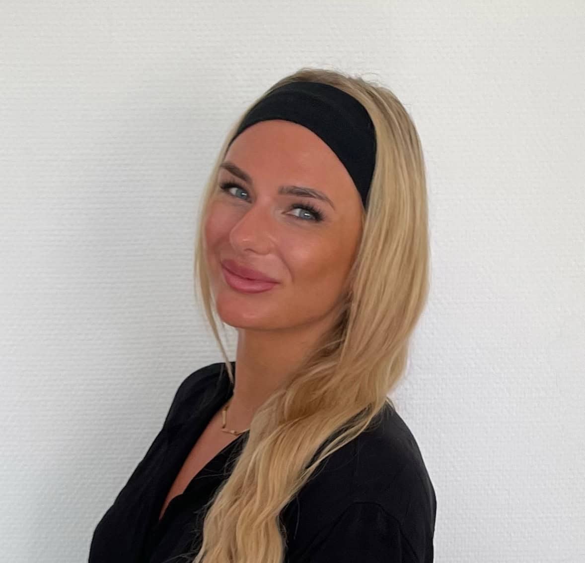 Porträt einer lächelnden Frau mit langem blondem Haar und schwarzem Stirnband.