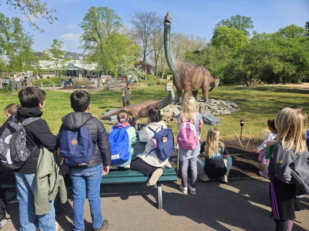 Kinder beobachten Dinosaurier-Modelle im Zoo bei schönem Frühlingswetter.