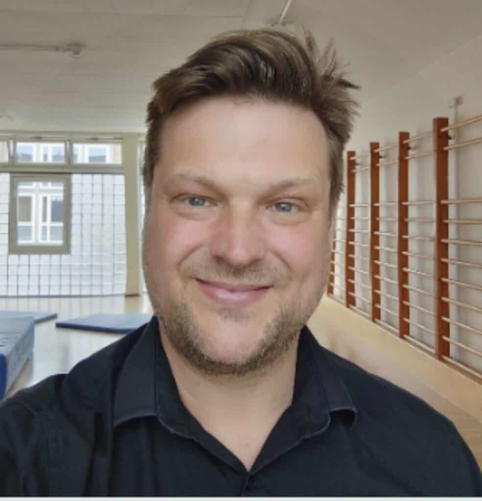 Mann lächelt in einem Raum mit Turngeräten im Hintergrund.